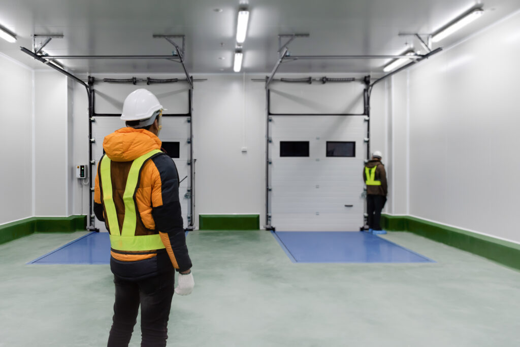Staff worker standing control inside loading room for goods in cold warehouse storage observing another worker at the loading dock door.
